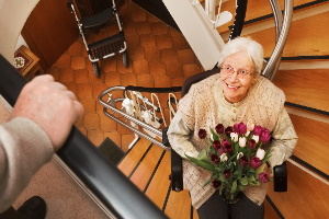 Ältere Frau mit Blumenstrauß auf einem Treppenlift