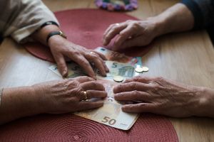 Hände älterer Menschen liegen auf Euro-Scheinen und Münzen auf einem Tisch.