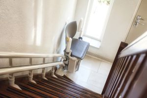 Ältere Frau mit einem Blumenstrauß auf einem Treppenlift.