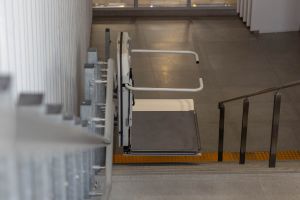 Zusammengeklappter Plattformlift (Rollstuhllift) neben einer Treppe.